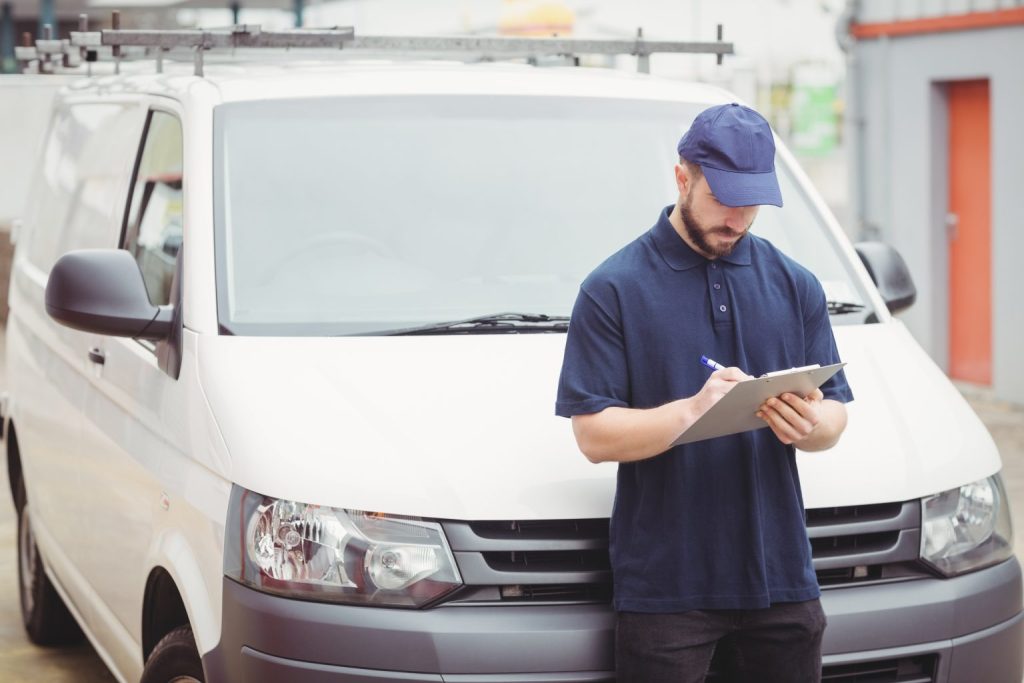 delivery-man-writing-on-clipboard-in-front-of-his-PN8KXER-1536x1024